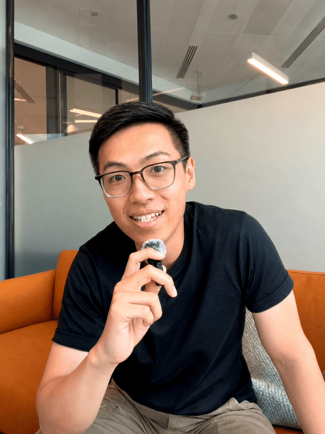 Harris Cheng smiling on a sofa, holding a wireless microphone